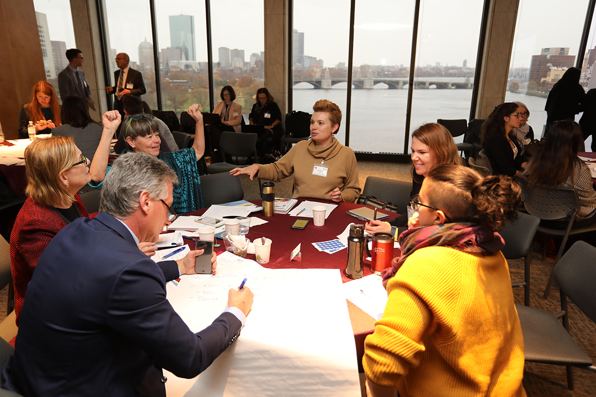 2019 summit event photo, people talking at table with Boston view