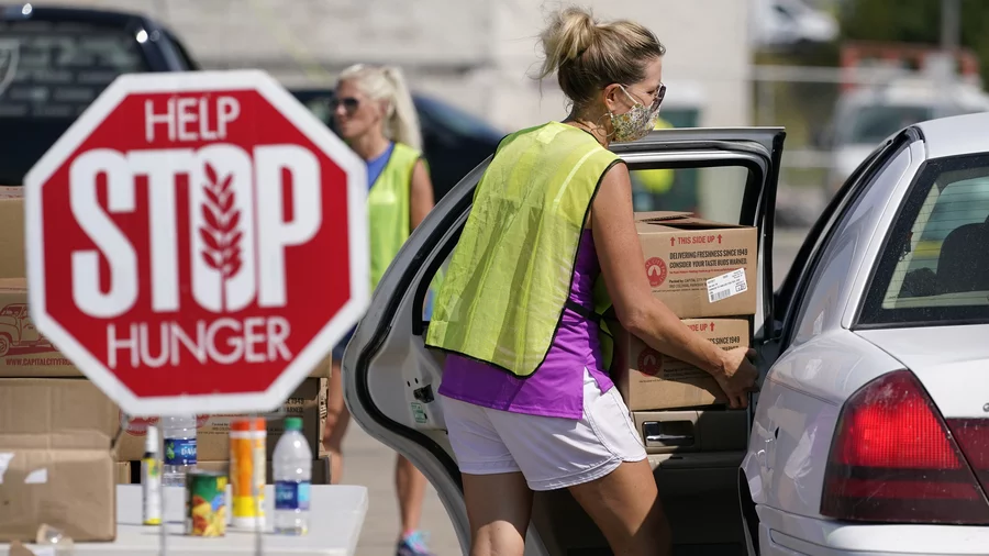 A volunteer loads a local resident's vehicle at a drive-up produce giveaway organized by a Des Moines food pantry on Aug. 28, 2020, in Des Moines, Iowa. Charlie Neibergall/AP
